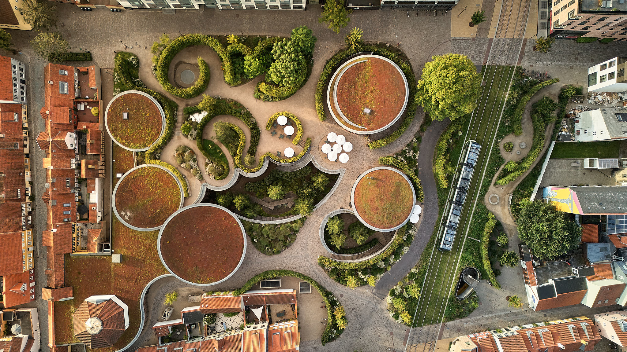 Luftfoto af moderne bypark med cirkulære grønne tage og røde mursten omkranset af bygninger